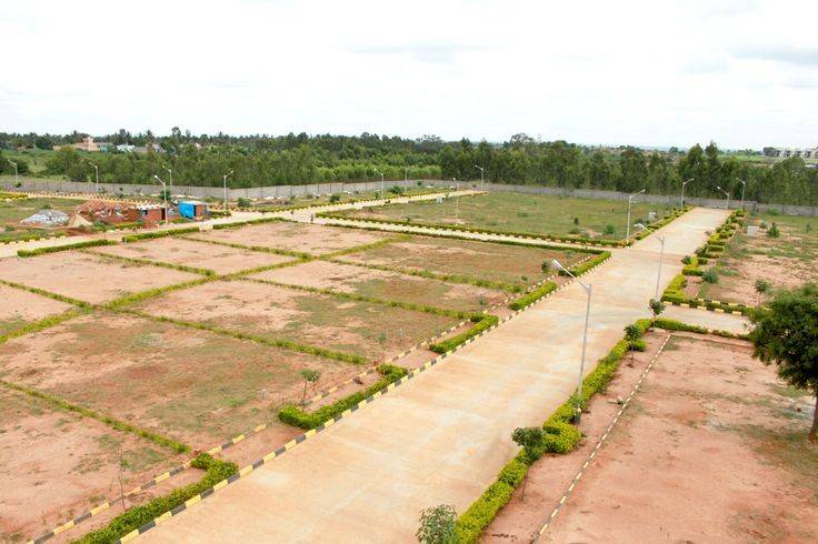 Aerial view of a green landscape with a grid of open plots, roads, and surrounding development